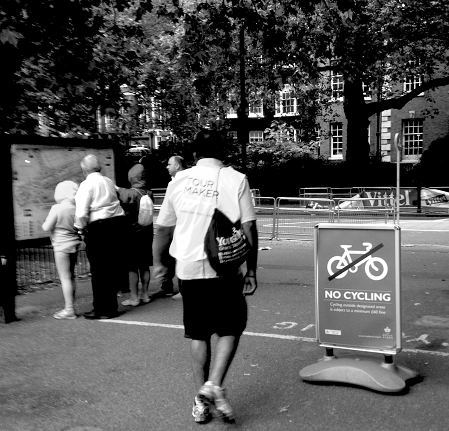 Mann mit "Tour Maker"-Weste vor Schild "No Cycling"
